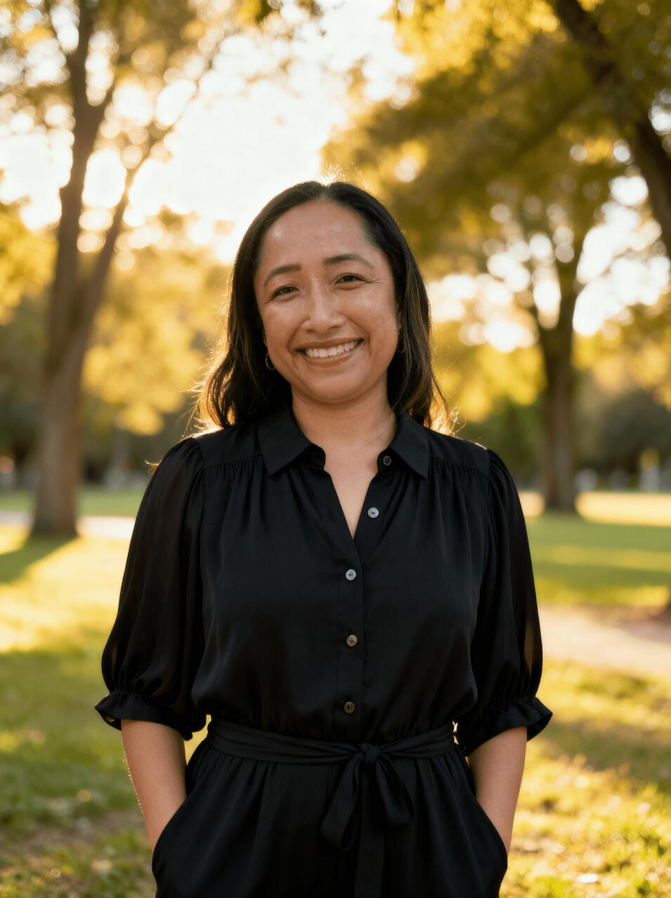 An image of a woman in a park, smiling at looking at the camera.